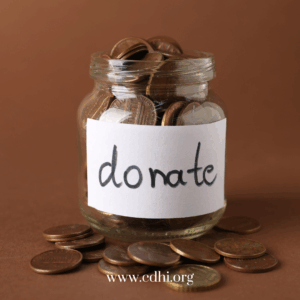 Donation jar filled with coins and a handwritten 'Donate' label; coins spill on the table, website www.cdhi.org visible at bottom.
