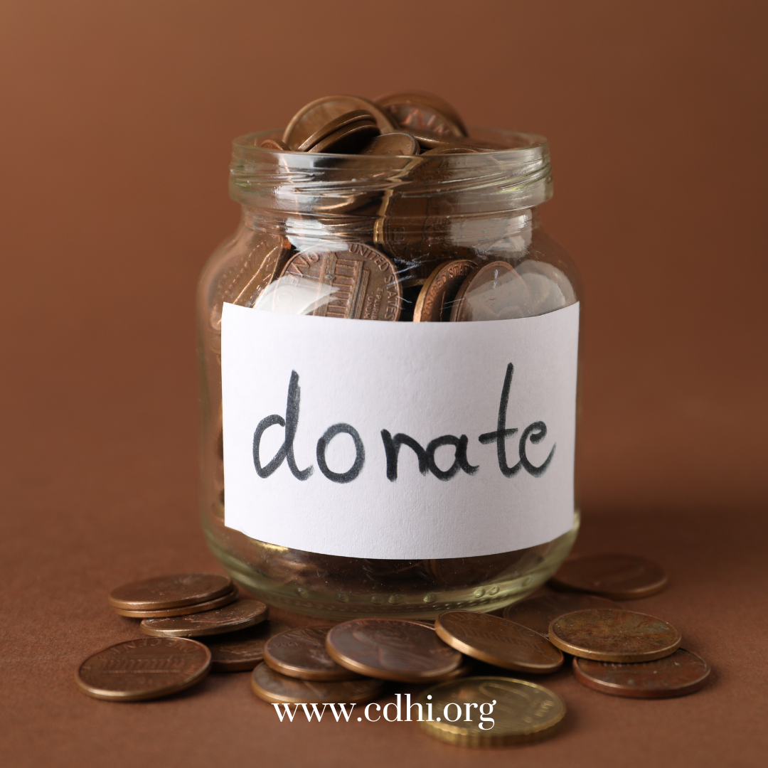 Donation jar filled with coins and a handwritten 'Donate' label; coins spill on the table, website www.cdhi.org visible at bottom.