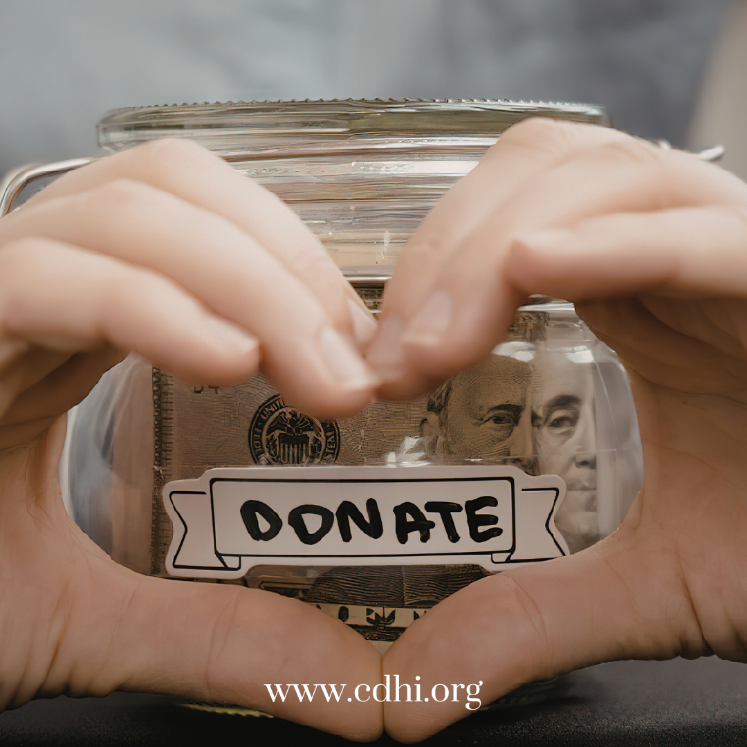 Hands frame a glass donation jar filled with money, with a DONATE label on the front.