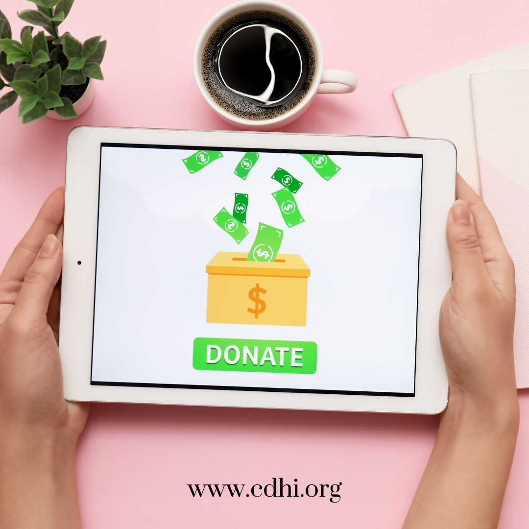 Tablet showing a donation graphic with a cash box and a green DONATE button on a pink desk.