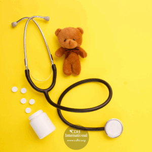 Pediatric medical scene: stethoscope, a brown teddy bear, pills, and a medicine bottle on a bright yellow background.