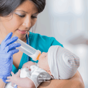 Nurse in teal scrubs and blue gloves feeds a newborn baby with a bottle.