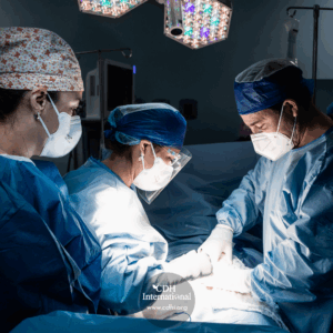Surgeons in blue scrubs and masks perform an operation around a patient on an illuminated operating table, with a CDH International watermark visible