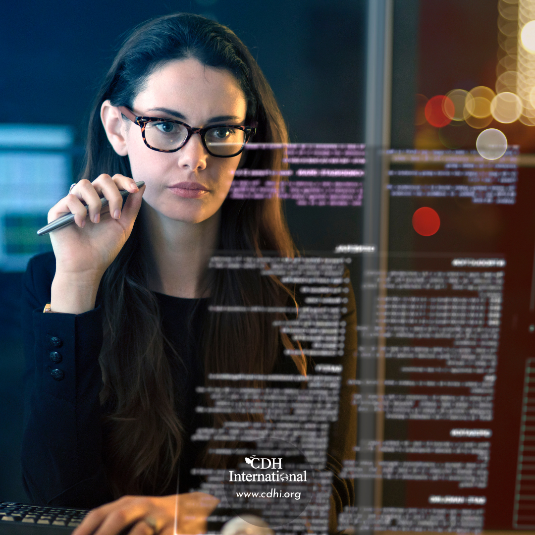 Woman with glasses examining lines of code on a transparent, glass-like display in a dark, modern office.
