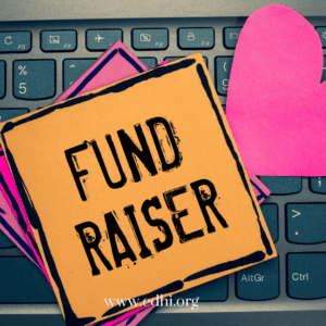 Orange sticky note on a laptop keyboard reading 'FUND RAISER' with pink paper hearts nearby.
